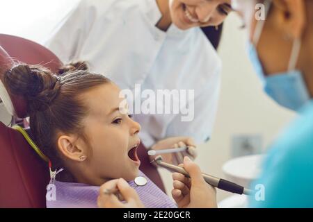 Petite fille allongé dans une chaise de dentiste et grinçant, n'ayant pas peur d'un examen de cavité buccale. Banque D'Images