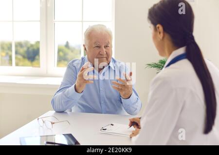 Une patiente âgée parle à une femme médecin tout en étant assise à une table dans un bureau d'hôpital. Banque D'Images