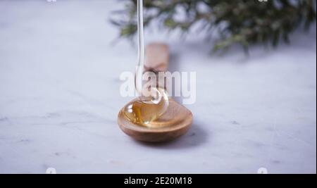 Flux de miel. Le miel doré, jaune, cru est en train de tomber de la louche de miel sur une cuillère à soupe de bois. Ingrédient sucré sain pour les cosmétiques naturels, les pâtisseries et Banque D'Images