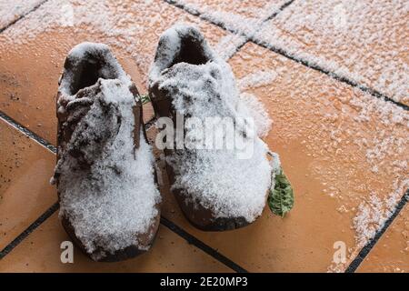 Une paire de chaussures couvertes de neige et de glace sur un sol carrelé dans l'arrière-cour d'une maison. Paysage d'hiver. Banque D'Images