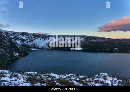 Magnifique coucher de soleil au-dessus de la crête enneigée près du pic d'Eagles Crag et du lac Lough Bray Lower dans des tons froids d'hiver, Co. Wicklow, Irlande. Hiver Irlande Banque D'Images