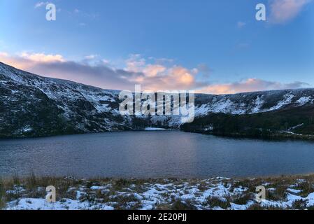 Superbe coucher de soleil au-dessus de la crête enneigée près du pic d'Eagles Crag et du lac Lough Bray Lower dans des tons froids d'hiver, Co. Wicklow, Irlande. Hiver Irlande Banque D'Images