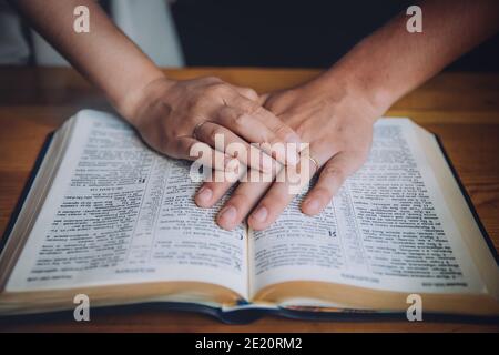 Couple de mariage ou couple plaçant leurs mains sur une bible ouverte. Il est possible de voir les bagues d'engagement dans leurs mains. Banque D'Images