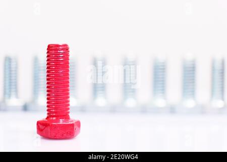 Gros plan du boulon rouge n un groupe de vis métalliques galvanisées. Leadership, individualité, notion de dissimilarité. Boulons en acier inoxydable isolés sur du blanc Banque D'Images