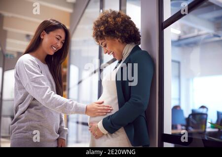 Femme d'affaires touchant des collègues femmes enceintes Bump dans le bureau moderne Banque D'Images