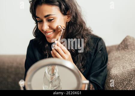 Belle brunette assise devant un miroir à l'aide du visage rouleau Banque D'Images