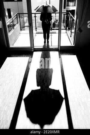 Femme avec un parapluie debout à l'intérieur d'une pièce vide contre une fenêtre avec la lumière du soleil en Suisse. Banque D'Images