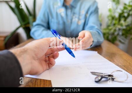 Un employé donne au client un stylo pour remplir les documents. Gros plan des mains. Il y a des papiers et des touches sur la table. Location et achat de biens immobiliers. Banque D'Images