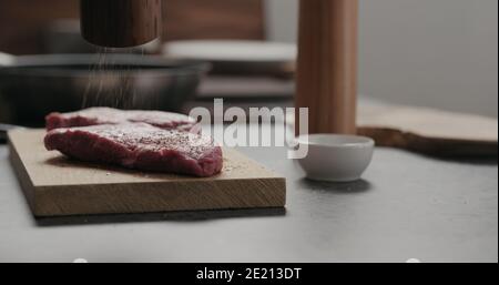 un homme meulant le poivre sur un steak de bœuf cru sur une planche de chêne, photo large Banque D'Images