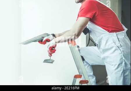 Travailleur caucasien dans ses années 30 avec Patching Tools dans sa main. Cloison sèche et préparation des murs intérieurs d'appartements pour la peinture. Travail de rénovation à la maison. Banque D'Images