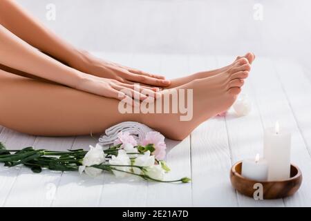 vue rognée de la femme avec les mains et les pieds soignés à proximité fleurs d'eustoma blanc et bougies sur une surface en bois blanc Banque D'Images