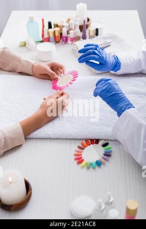 vue rognée de la femme tenant une palette de faux ongles près fournitures de manucure et de manucure sur fond flou Banque D'Images