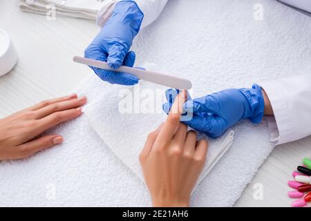 vue partielle du manucure dans des gants en latex à l'aide d'une lime à ongles tout en faisant la manucure à la femme Banque D'Images