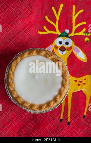 Tarte aux pommes de terre hachée glacée de Sainsburys sur une serviette de Noël festive - pâtisseries fourrées de viande hachée, recouvertes de glaçage blanc doux Banque D'Images