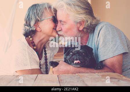 Les personnes âgées de race blanche coupent baiser et aimer ensemble avec le noir chien pug au milieu - portrait de l'homme heureux et les femmes âgées style de vie à la maison - f Banque D'Images