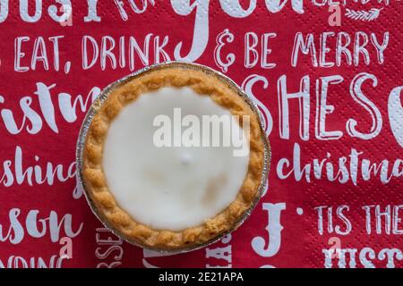 Tarte aux pommes de terre hachée glacée de Sainsburys sur une serviette de Noël festive - pâtisseries fourrées de viande hachée, recouvertes de glaçage blanc doux Banque D'Images