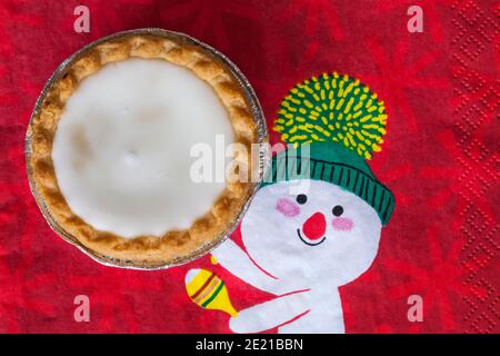 Tarte aux pommes de terre hachée glacée de Sainsburys sur une serviette de Noël festive - pâtisseries fourrées de viande hachée, recouvertes de glaçage blanc doux Banque D'Images