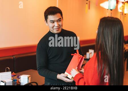 Beau jeune couple asiatique en vêtements rouges donner présent dans le restaurant chinois vietnamien festif lanternes en papier coloré, célébrant le nouvel Yea chinois Banque D'Images