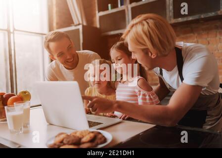 Couple gay avec leurs filles adorables adoptées lisant la recette sur ordinateur portable et la cuisine sur la cuisine. La famille LGBT à la maison. Banque D'Images