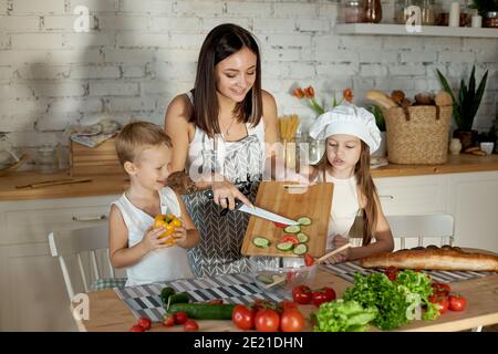 Maman cuisine le déjeuner avec les enfants. Une femme enseigne à sa fille la cuisine de son fils. Végétarisme et alimentation naturelle saine Banque D'Images