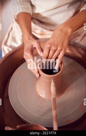 Gros plan de la gaine de mise en forme femelle Potter pour Pot On Roue de poterie dans le studio de céramique Banque D'Images