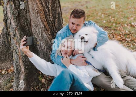 Bonne jolie dame tenant un smartphone assis avec son petit ami et chien dans le parc Banque D'Images