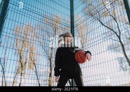 Vue basse d'une femme sportive dans une tenue de sport noire un ballon de basket tout en regardant loin Banque D'Images