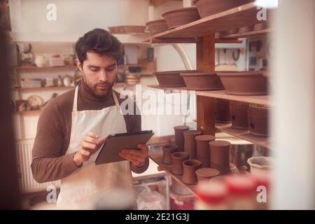 Potter masculin dans Ceramics Studio contrôle des commandes à l'aide de la tablette numérique Banque D'Images