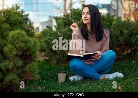 Agréable étudiante assise sur l'herbe avec ses pattes croisées et le stylet et l'ordinateur portable Banque D'Images