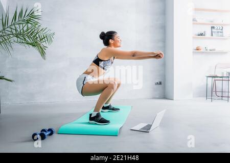 jeune sportif afro-américain faisant des sit up près d'un ordinateur portable et haltères Banque D'Images