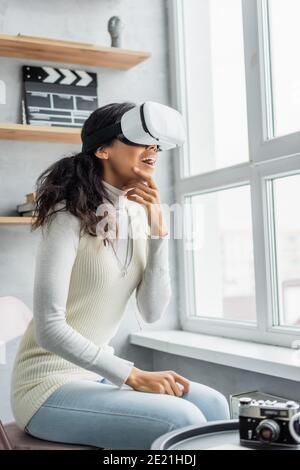 une femme afro-américaine excitée dans un casque vr regardant par la fenêtre appareil photo d'époque sur un premier plan flou Banque D'Images