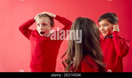 Groupe d'élèves enthousiastes de l'école élémentaire portant un uniforme ayant du plaisir Sur fond Red Studio Banque D'Images