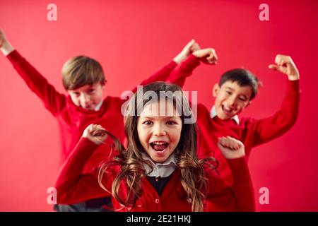 Portrait des élèves enthousiastes de l'école primaire portant un uniforme ayant du plaisir Sur l'arrière-plan Red Studio Banque D'Images