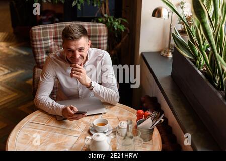 Vue de dessus d'un jeune homme d'affaires heureux en utilisant un smartphone tout en étant assis à la table dans le café. Concept de style de vie Banque D'Images