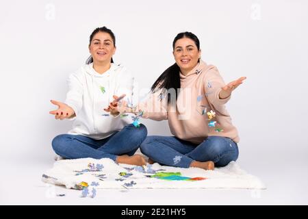 Des jumeaux sur le sol, assis sur une couverture douce, souriez et jetez le puzzle dans l'appareil photo. Arrière-plan blanc. Banque D'Images