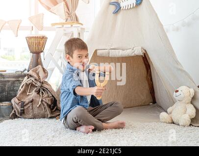 Petit garçon avec une langire de bois assis sur le sol de la chambre à l'intérieur avant du wigwam Banque D'Images