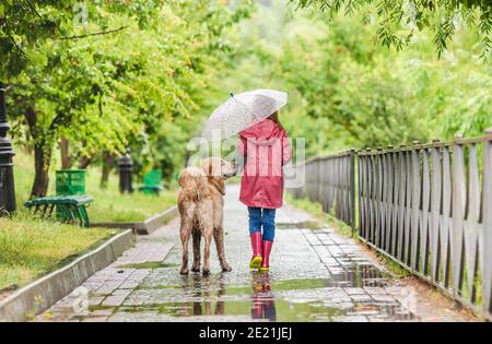 Vue arrière de la petite fille marchant chien sous la pluie le long allée humide Banque D'Images