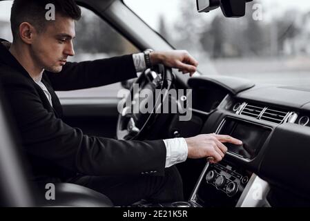 Photo rognée d'un jeune homme charmant qui appuie sur le pavé tactile tout en conduisant une voiture dans la ville. Concept de location et de reprise Banque D'Images