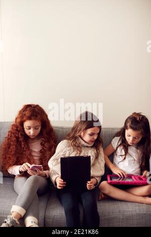 Groupe de filles avec des amis assis sur un canapé à la maison Lecture sur une tablette numérique et un téléphone portable Banque D'Images