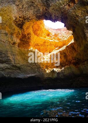 Le soleil traverse un trou de la grotte de Benagil, au Portugal, donnant une spectaculaire couleur bleue à l'eau de mer. Banque D'Images