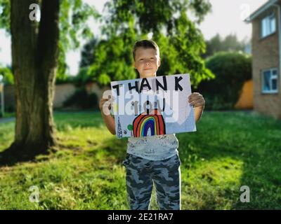 Un jeune garçon tient un dessin arc-en-ciel et le remerciement Message pour le personnel médical travaillant par le biais du Covid-19 Pandémie Banque D'Images