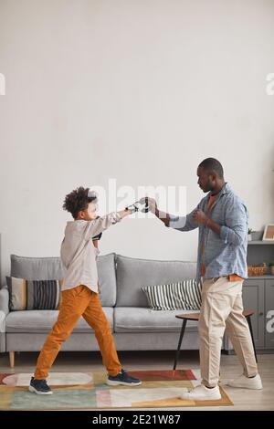 Un père afro-américain moderne pratique des punchs de boxe avec son fils adolescent dans le salon à la maison, vue latérale verticale longue vue Banque D'Images