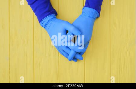 Les mains gantées bleues se rapprochent sur fond de bois jaune. Demandez la désinfection des mains. Arrêter le concept du coronavirus. Utilisation de gel antibactérien pour les mains pendant Banque D'Images