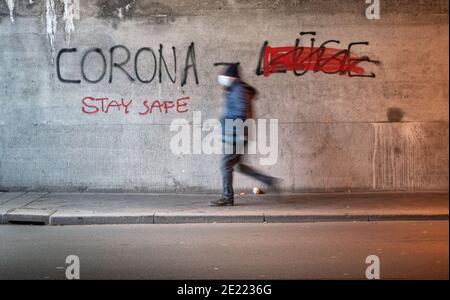 Offenbach, Allemagne. 11 janvier 2021. Un homme portant un protecteur de bouche-nez traverse un passage souterrain de chemin de fer d'Offenbach avec « Corona lie » écrit sur le mur, avec de la peinture rouge traversant le mot peint en aérosol « lie » (r). Au lieu de cela, 'Stay Safe' a été pulvérisé sous le mot 'Corona'. Credit: Frank Rumpenhorst/dpa/Alay Live News Banque D'Images