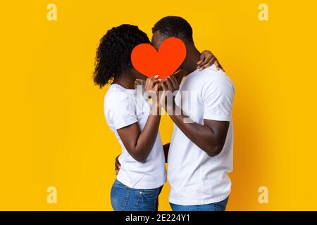 Couple afro-américain embrassant et se cachant derrière le cœur rouge Banque D'Images