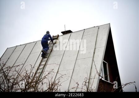 Le couvreur de toit monte l'échelle jusqu'au toit de la maison pour fixer le toit en tôle Banque D'Images