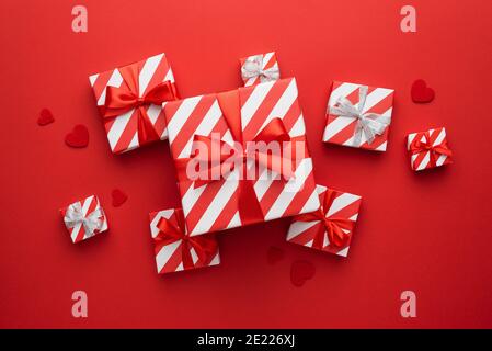 Carte de Saint-Valentin avec boîtes de cadeaux emballées dans un emballage papier avec ruban rouge et boucles sur fond rouge avec cœurs Banque D'Images