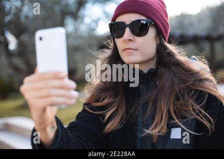 Femme portant un bonnet rouge et des lunettes de soleil prenant un selfie à l'extérieur Banque D'Images