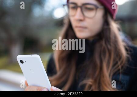 Femme portant un bonnet et des lunettes rouges à l'aide d'un téléphone portable extérieur Banque D'Images