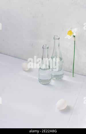 Encore la vie avec des bouteilles, des oeufs et des fleurs. Arrière-plan blanc. Concept minimal. Banque D'Images